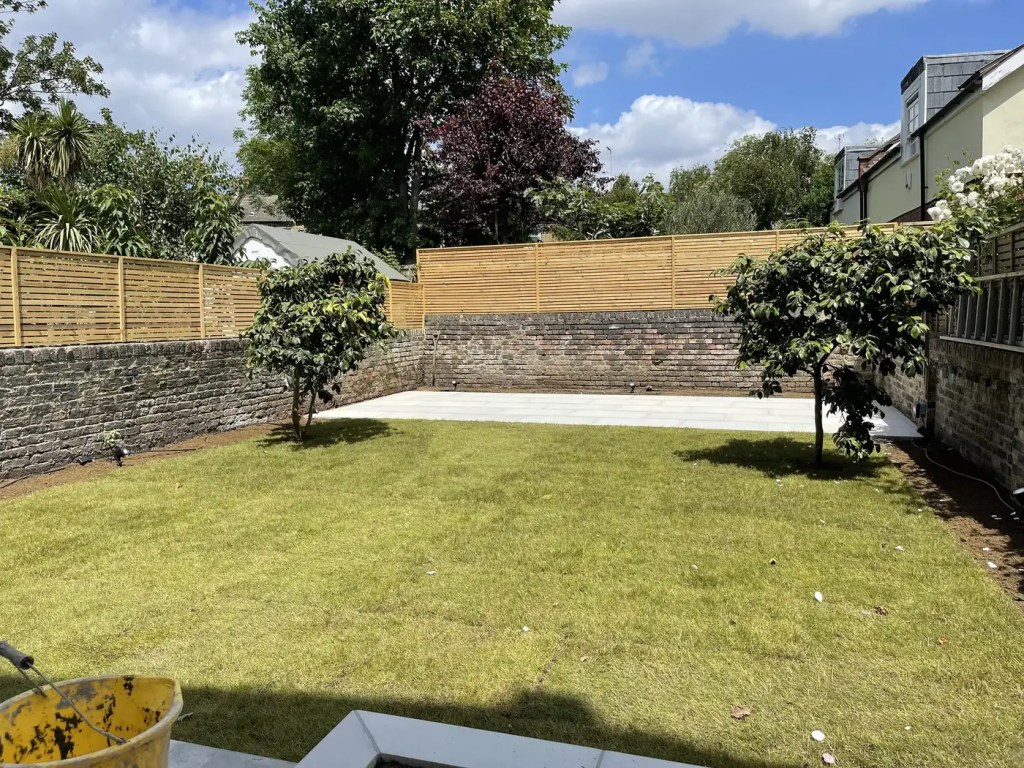 New lawn with timber fencing and paved terrace in a completed South London garden.