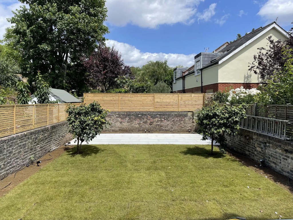 Newly installed lawn with timber fencing and a paved seating area in a South London garden.