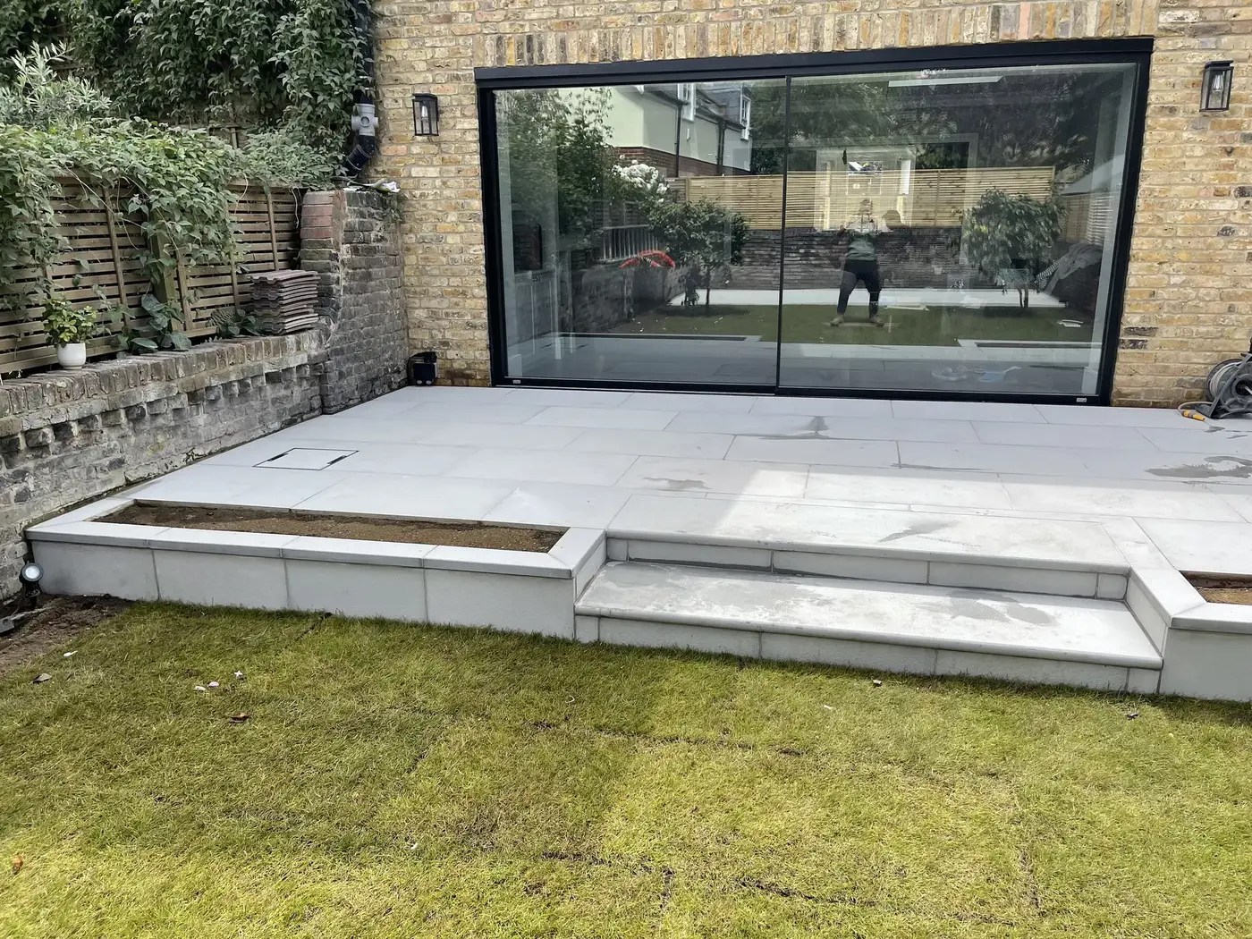 Completed landscaped garden with stone patio, steps, lawn and timber fencing in South London.