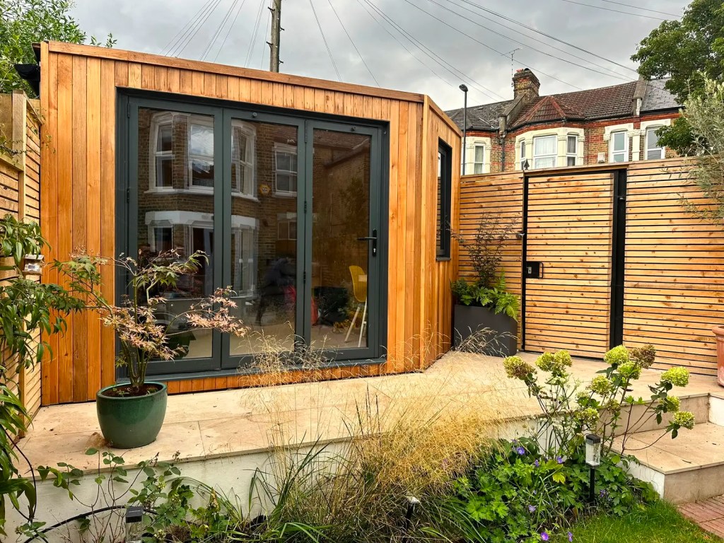 Close view of a bespoke timber-clad garden room with dark framed glazed doors.