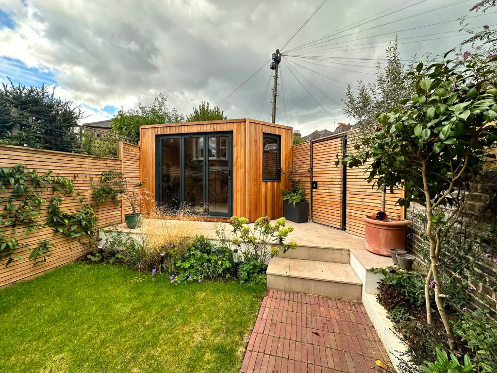 Bespoke timber garden room integrated with planting, lawn, paving and fencing in a South London garden.